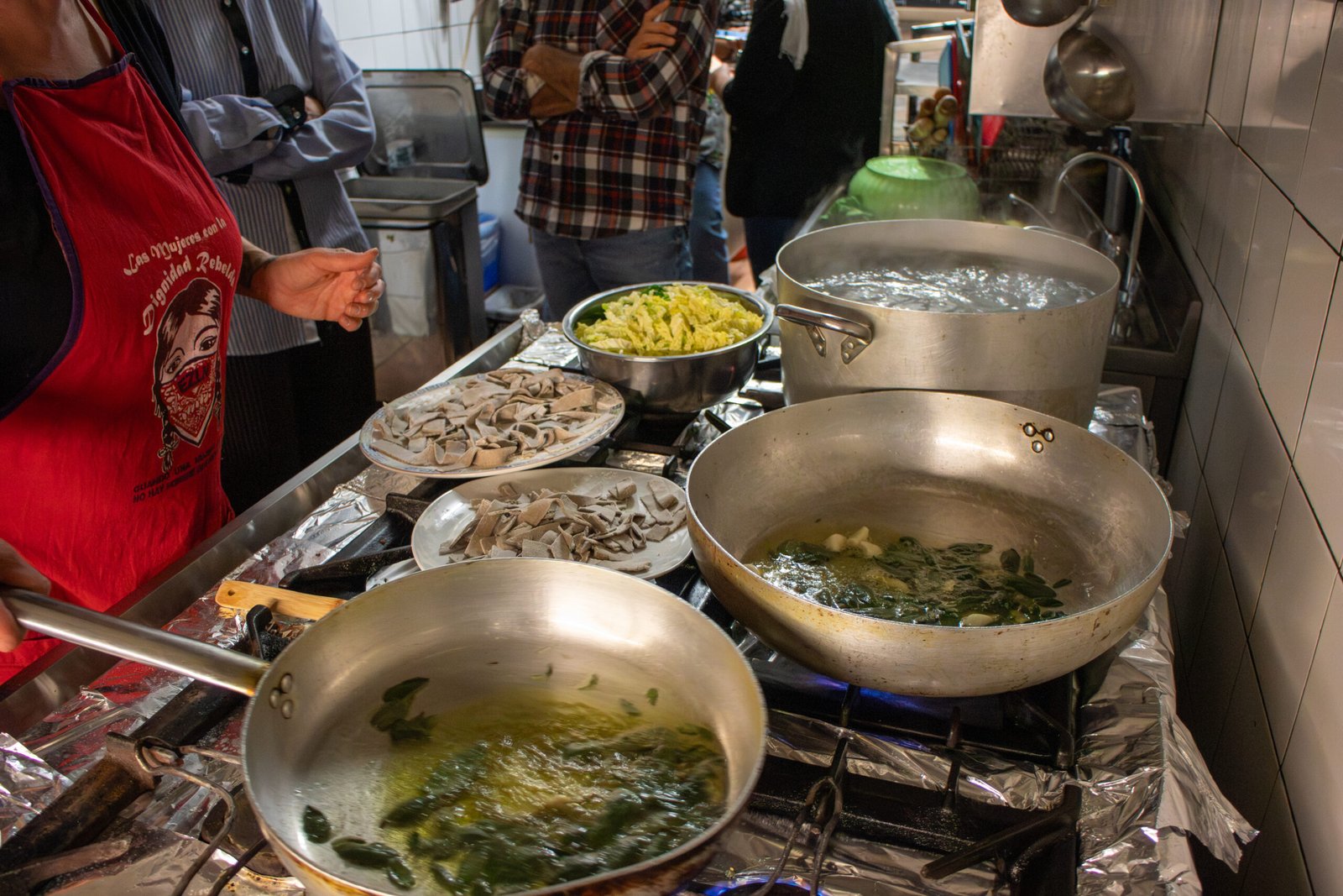 Padelle sui fornelli con verdure in cottura e piatti di pasta fresca appena tagliata