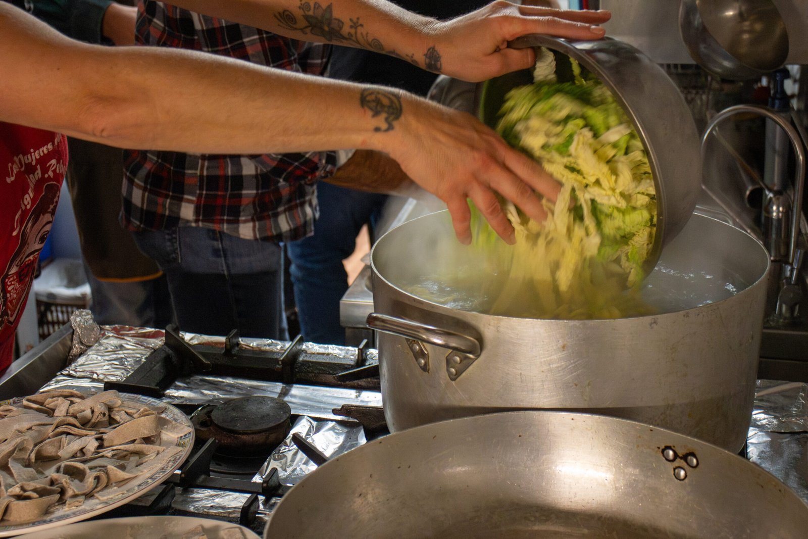 Le mani di due partecipanti versano la verdura tagliata in una pentola d'acqua bollente